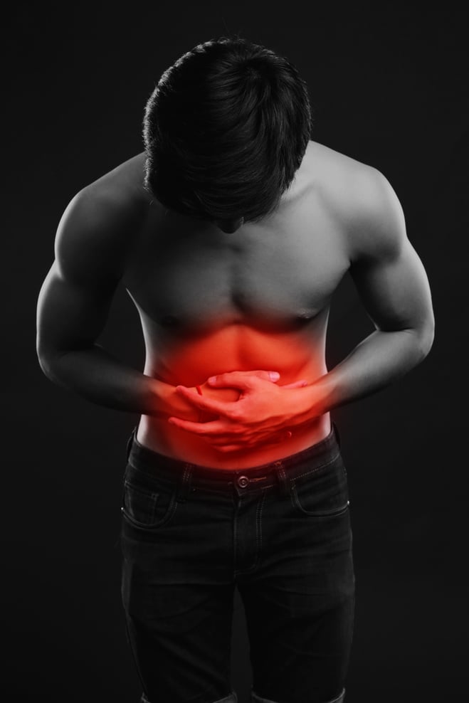 Young man holding his sick stomach in pain on black background